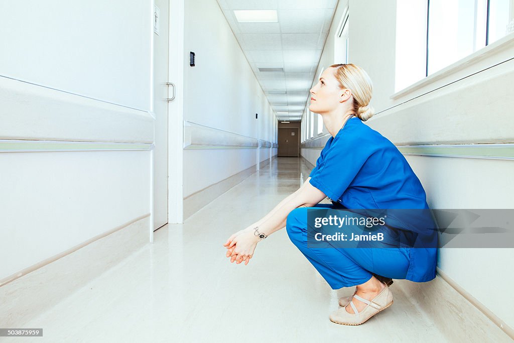 Tired doctor crouching in hospital corridor