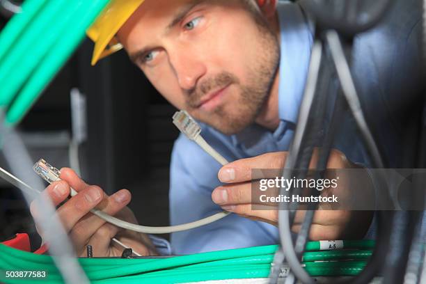 network engineer examining patch cable under patch panel - tomada de ligação à rede imagens e fotografias de stock