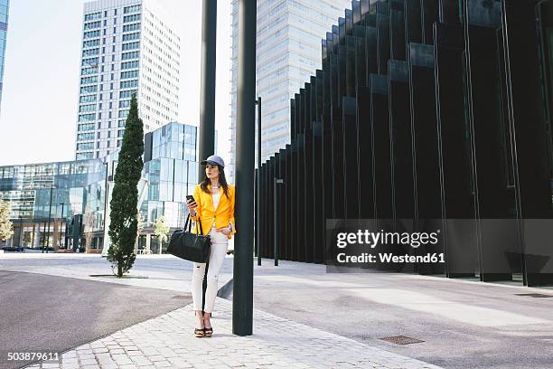 spain,catalunya, barcelona, young modern woman with yellow jacket leaning against street lamp - hands in pockets stock pictures, royalty-free photos & images