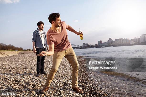 two friends skipping stones at river - skimming stones stock pictures, royalty-free photos & images