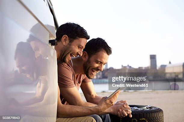 two laughing men sitting in car looking at digital tablet - automobile and fun fotografías e imágenes de stock