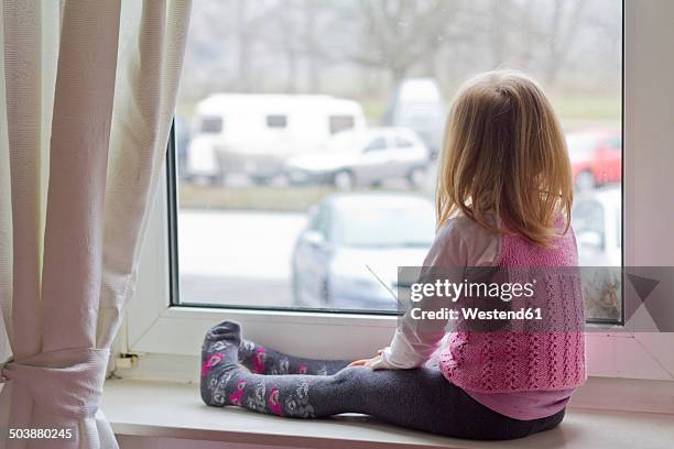 little girl sitting on window sill looking out of window - girl side view stock-fotos und bilder