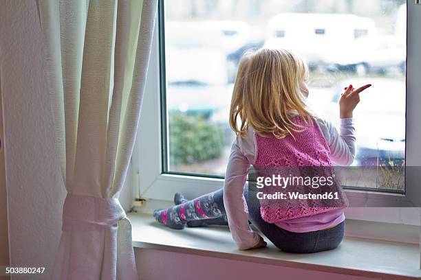 little girl sitting on window sill looking out of window - girl pointing stock-fotos und bilder