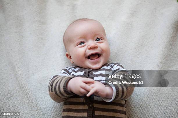 portrait of laughing baby boy lying on blanket, view from above - baby stock-fotos und bilder