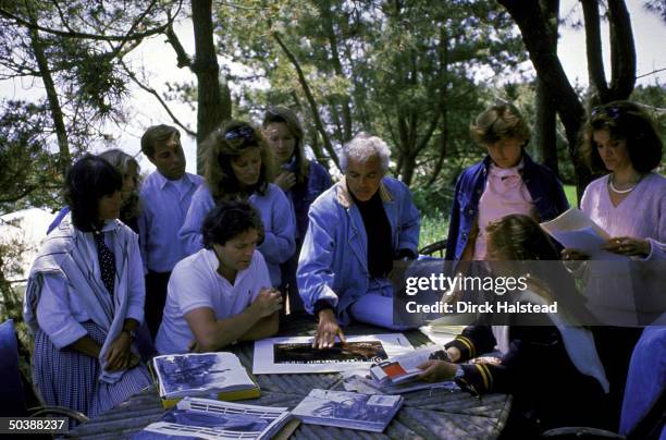 Fashion Designer Ralph Lauren sitting on picnic table with his staff looking over fall ads.