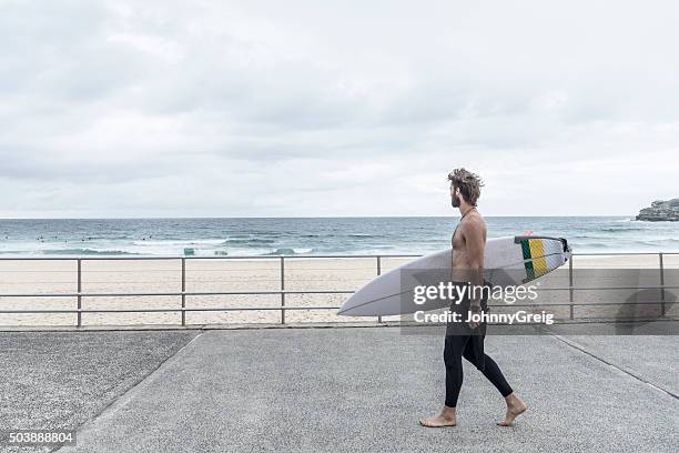 man carrying surfboard along promenade, bondi beach - promenade seafront stock pictures, royalty-free photos & images