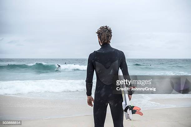 surfer holding surfboard on bondi beach, rear view - surfer wetsuit stockfoto's en -beelden