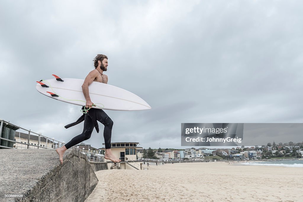 Man leaping off wall with surfboard, Bondi Beach