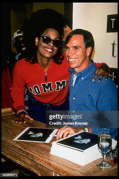 Fashion designer Tommy Hilfiger w. Rap singer/model Spinerella w. Stack of his publicity portraits at autograph party to launch his new women's...