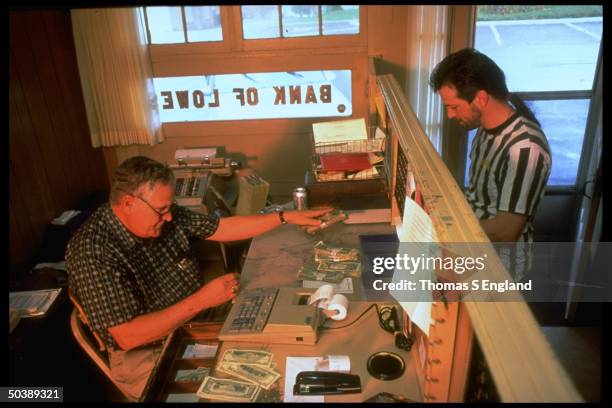 Bank teller Jack Wilkerson w. Currency at counter of bank windo while serving customer Andrew T.C. Wilson at the Bank of Lowes, founded in 1904,...