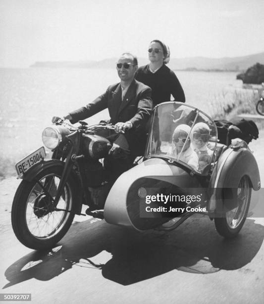 Man and woman riding a motorcycle with three children tucked into the attached side car on a family trip in Italy, July 1954.