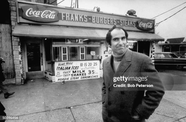 Author, Philip Roth, revisiting areas where he grew up in Newark, standing at hamburger stand.