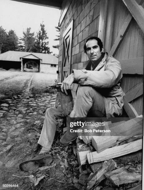 Author of Portnoy's Complaint, Philip Roth, sitting on wood pile.