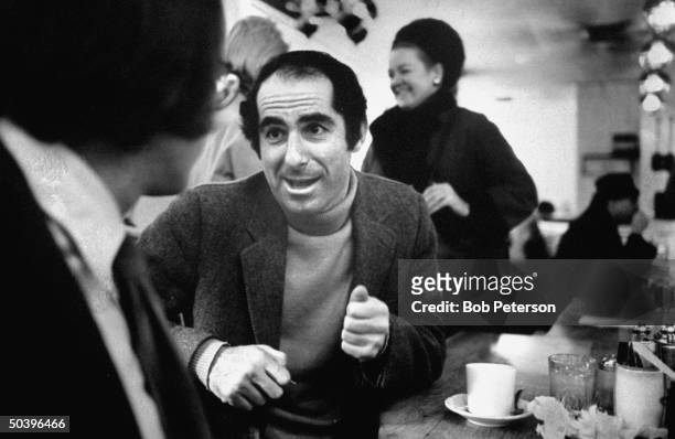 Author, Philip Roth, revisiting areas where he grew up, sitting at lunch counter talking with a customer.