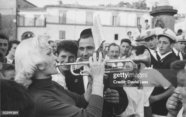 Singer Juli Reding learning how to play a trumpet, while appreciative males look on, during her visit.