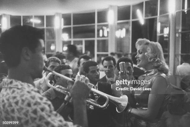 Singer Juli Reding singing for a group of fans as a man plays the trumpet.