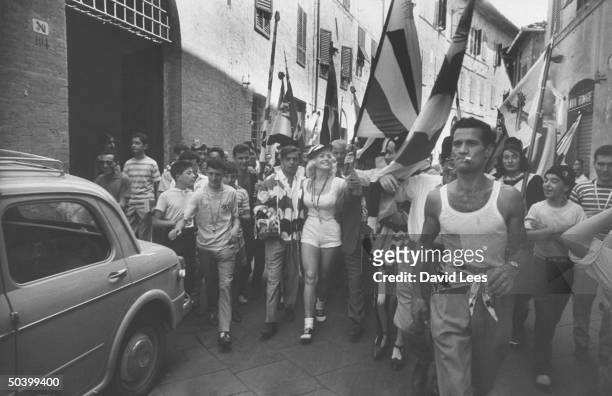 Singer Juli Reding wearing shorts, carrying an Italian flag while walking down the street wth a group of fans .