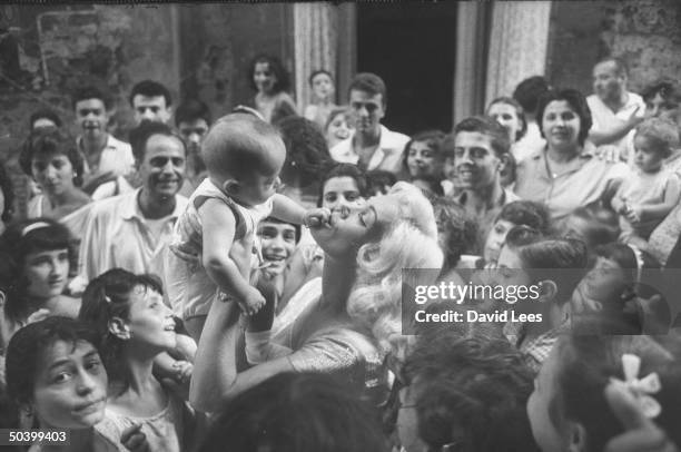 Singer Juli Reding holding and kissing a baby while fans crowd around her.