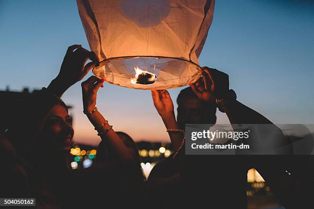 friends releasing paper lantern in the sky at night - hot air balloon people stock pictures, royalty-free photos & images