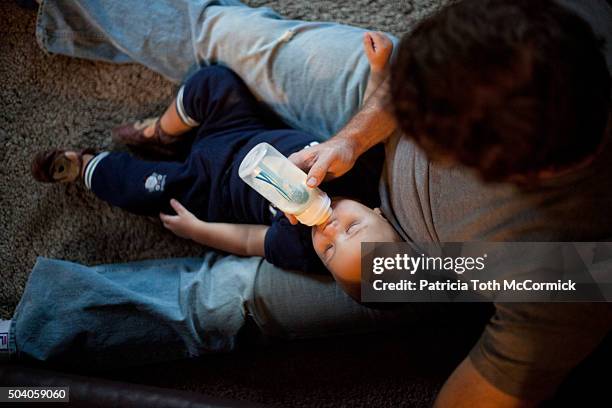 man feeding infant boy a bottle - baby bottle stock pictures, royalty-free photos & images