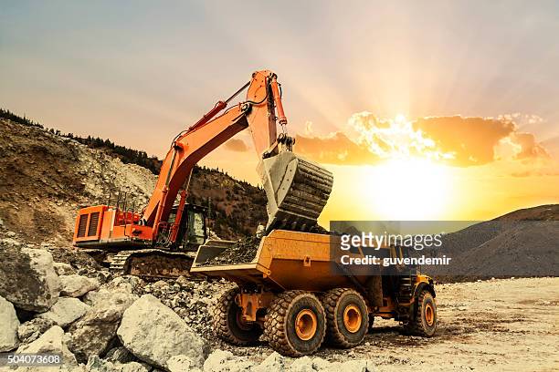 excavator loading dumper truck on mining site - mining natural resources stock pictures, royalty-free photos & images
