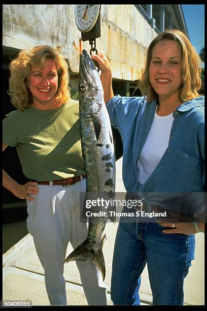 Reporters Meg Grant & Cindy Dampier holding fish they caught while covering story of secret wedding of GEORGE editor John F. Kennedy Jr. & publicist...