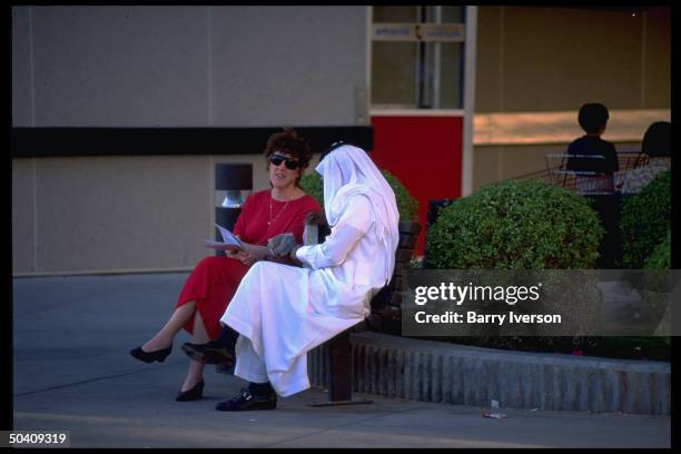 American woman chatting w. Saudi man, sitting outside Aramco oil Dhahran Commissary .