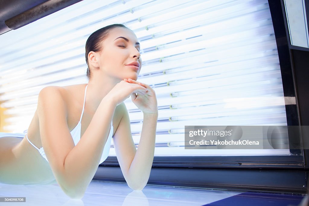 Cheerful young woman is getting treatment in solarium