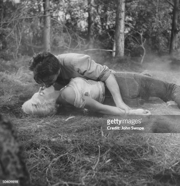 Actor Robert Mitchum kissing Marilyn Monroe as he wrestles with her on the ground in scene from film, River of No Return.