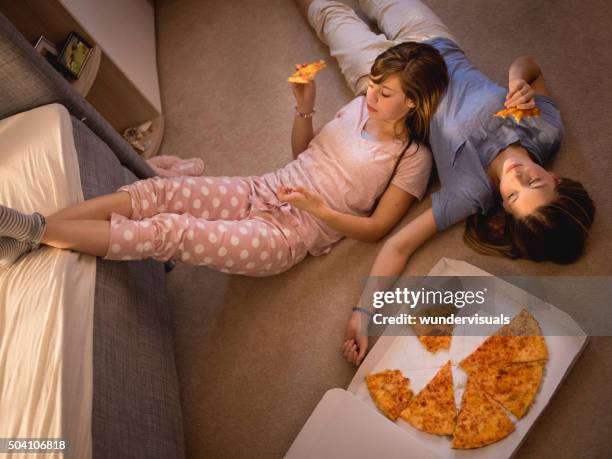 teen girls eating pizza while lying on a bedroom floor - pyjamas stock pictures, royalty-free photos & images