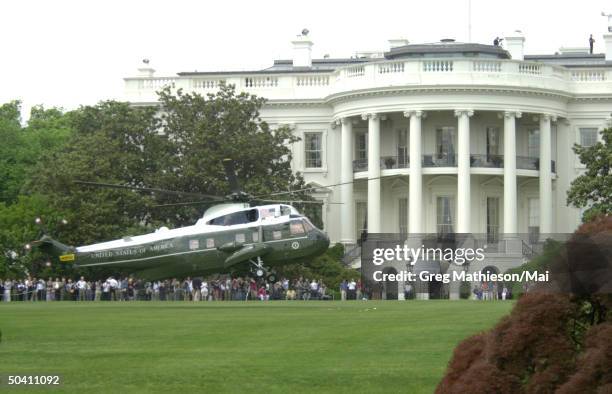 President George W. Bush arriving via Marine One on the South Lawn of the White House while guests and members of the press await in the background.