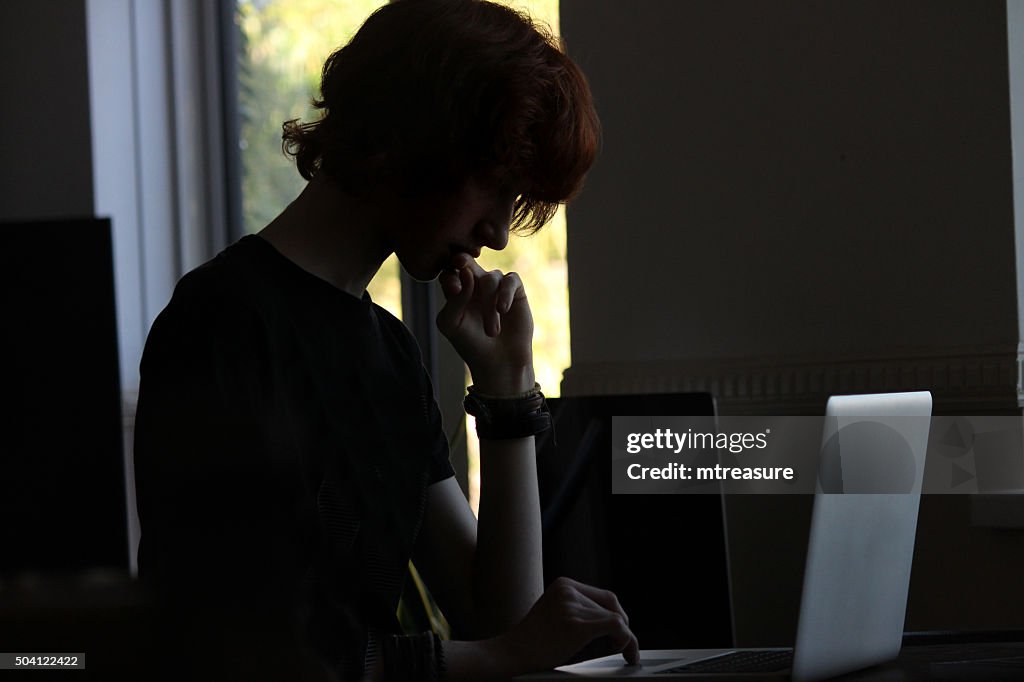 Image of teenage boy / hacker silhouette sat by laptop computer