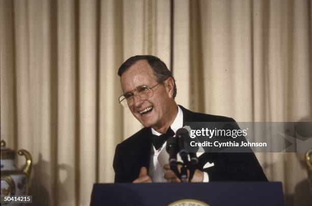 President George Bush in black tie, laughing at podium during speech at the Wilson Scholars dinner.