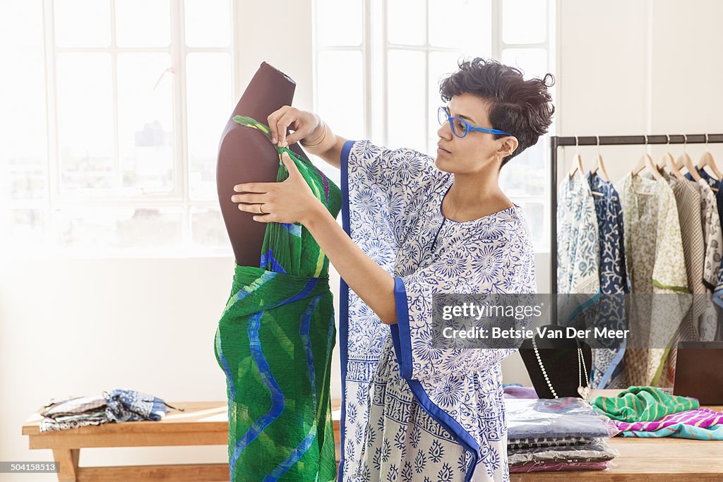 Fashion designer working on dress on dummy .