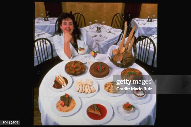 Chef Joan Winters posed sitting at a round table w. Various Italian-American deserts on it at the Duane Park Cafe.