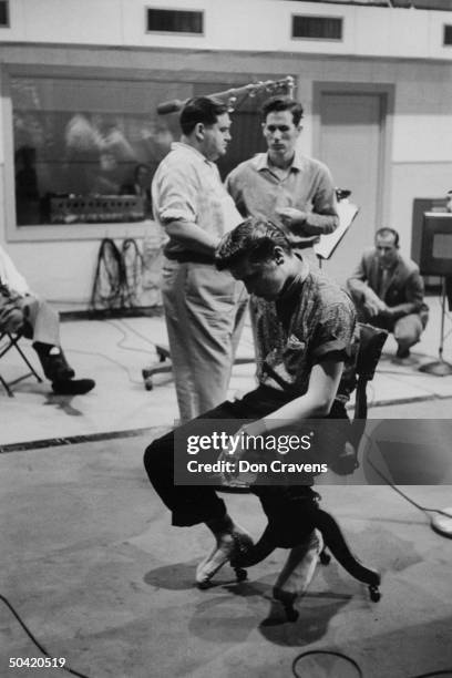 Singer Elvis Presley, in stocking feet and looking tired and somewhat dejected, sitting in chair during break from recording new record at the RCA...