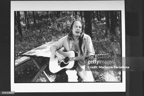 Author Rock Brynner sitting at picnic table, playing his guitar & singing, at home.