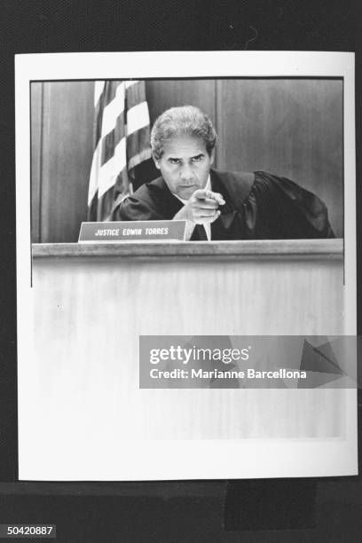 Supreme Court judge/author Edwin Torres wearing judicial robe, pointing an accusing finger as he presides during trial in courtroom.