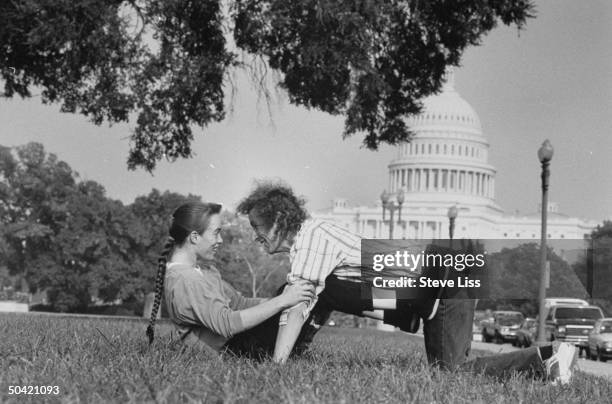 Astronomer/computer mgr. Cliff Stoll posing playfully w. His wife Martha Matthews in park in front of US Capitol bldg.