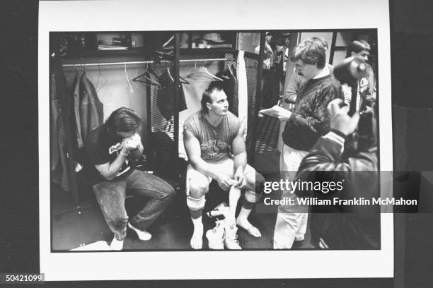 Green Bay Packers offensive lineman Tony Mandarich in uniform, sitting on bench, preparing to put on his shoes & socks as reporter w. Pad & pencil...