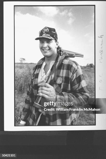 Green Bay Packers offensive lineman Tony Mandarich, sporting hunting clothes, posing w. A double-barreled shotgun broken open, draped over one...