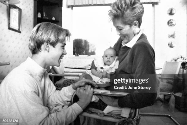 Teen actor Mark Paul Gosselaar watching as his mother holds her granddaughter in kitchen.