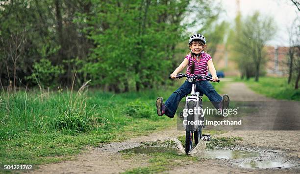 little girl équitation un vélo dans une flaque. - riding photos et images de collection