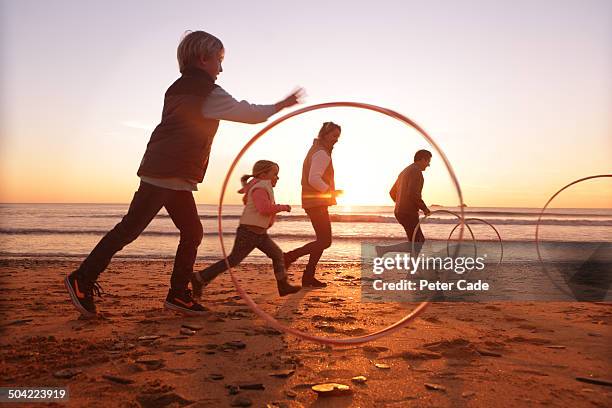 family playing with hoops on beach at sunset - gymnastikreifen stock-fotos und bilder