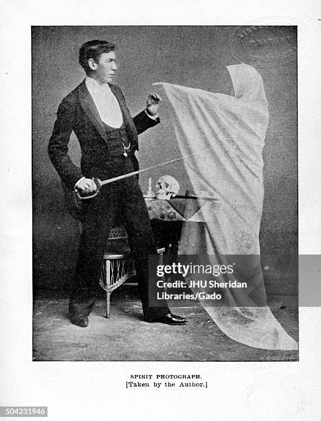 Spirit photograph showing man in formal suit holding a saber and reaching out his hand to touch the hand of a ghost in a white cloak who hovers above...