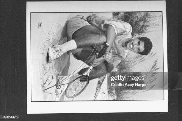 Open tennis champ Pete Sampras wearing t-shirt & shorts, holding a wooden Wilson tennis racket as he poses on isolated sandy beach.