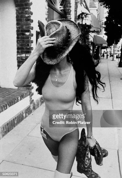 Singer Cher, wearing leotard and fishnet stockings, covering face w. Straw hat while shopping in Beverly Hills, CA.