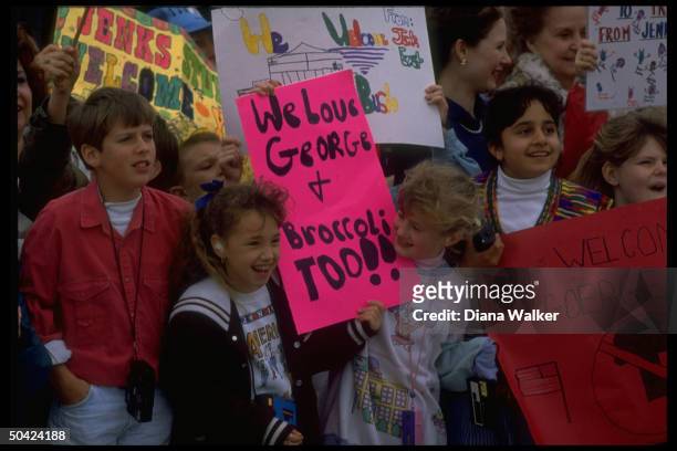 Schoolchildren out to greet Pres. Bush w. Signs incl. In re his decision to ban broccoli fr. Presidential table .
