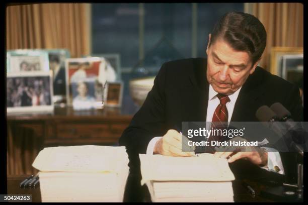 Pres. Reagan signing budget & reconciliation bill in WH Oval Office.