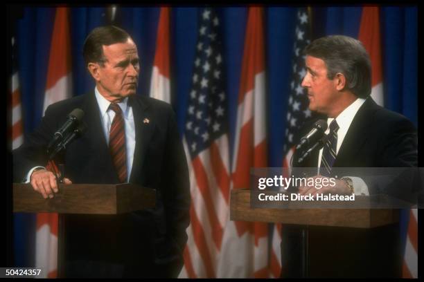 Pres. Bush & his host PM Brian Mulroney speaking to press against US & Canadian flags backdrop.